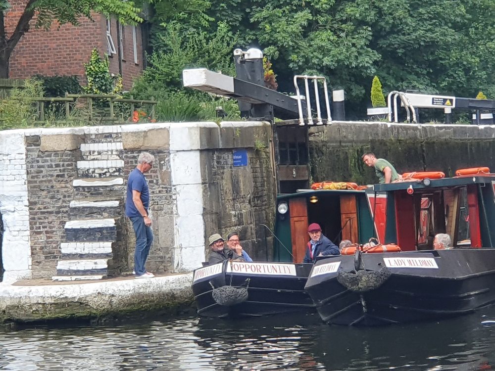 Two canal boats with members of the geezers already on board pass Eddie stood on the bank by the lock.