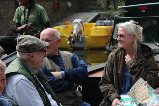 Three people (Ray Gibson, Carolyn Clark and other) sit on a canal boat in sunshine.