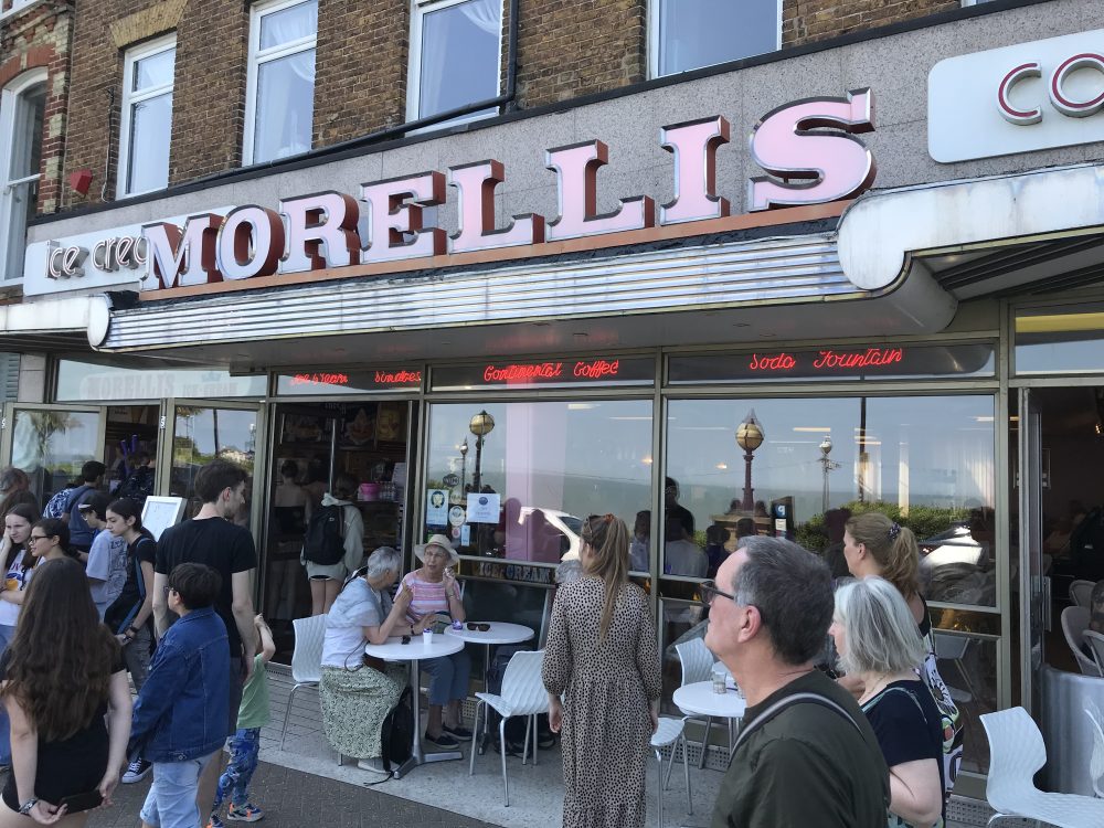 Ice Cream shop with a large group of people in front. Morellis written in bold letters above the shop entrance.