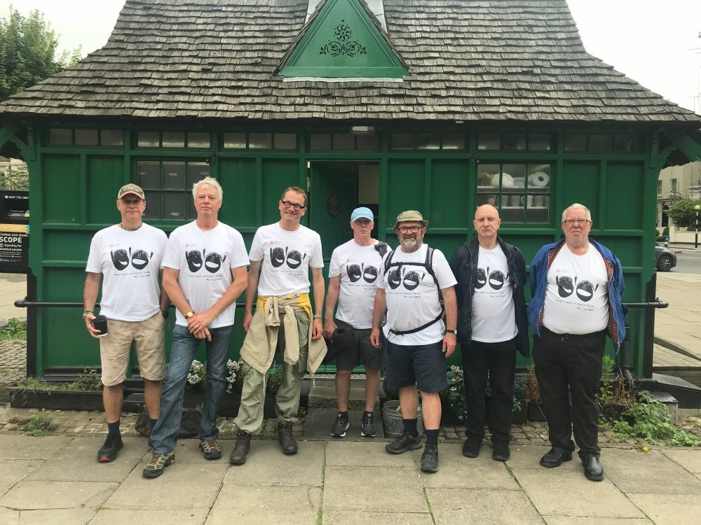 Group poses in front of small green building. All wearing matching white t-shirts with the Headway logo.