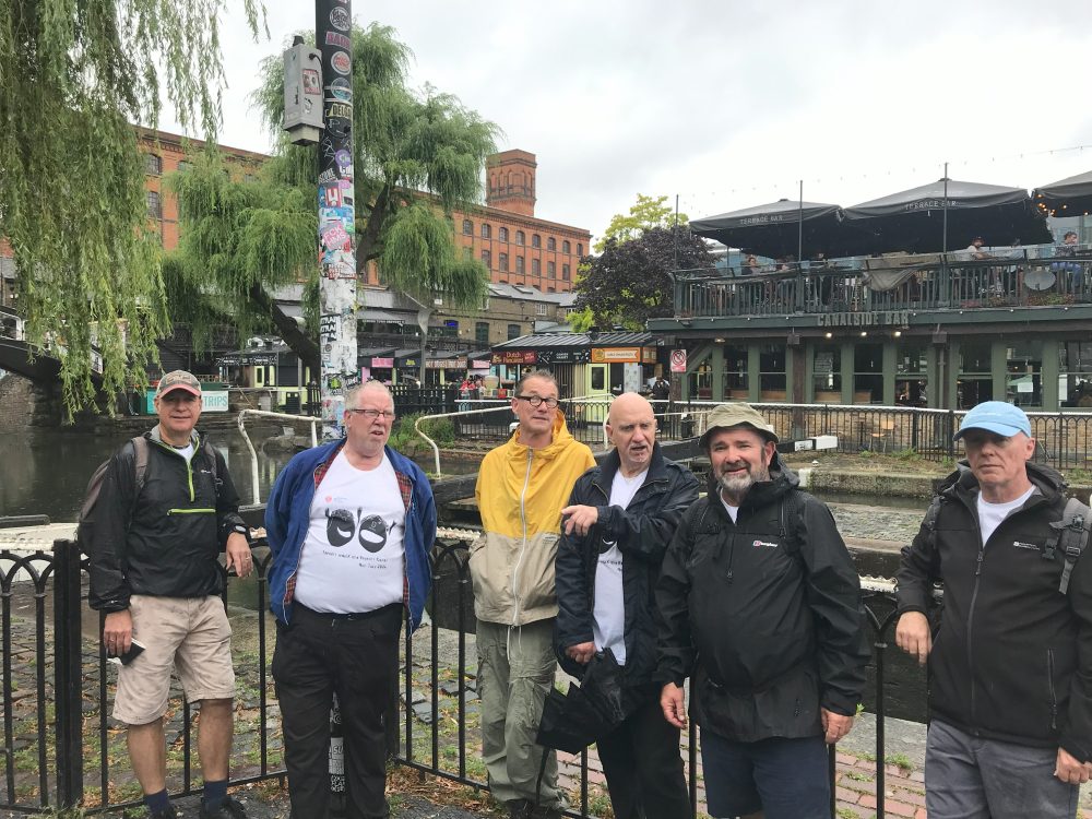 Group poses in front of a canal lock. Wearing rain jackets.