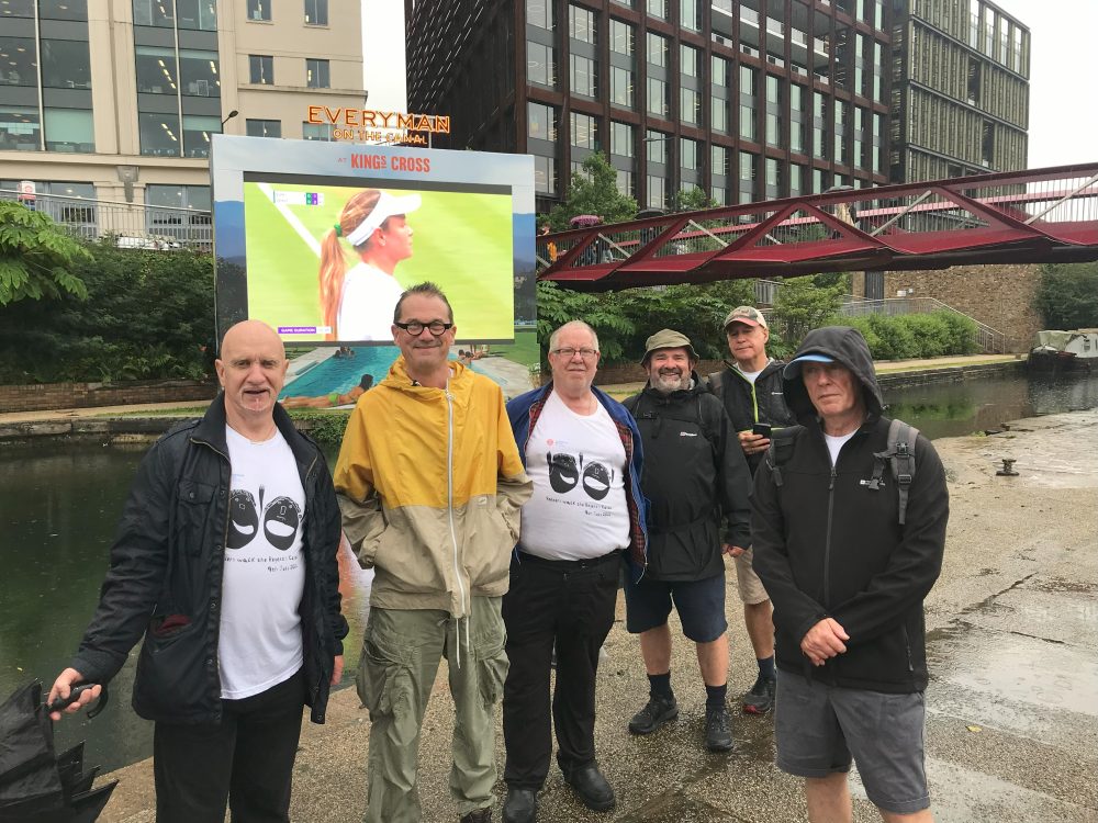 Group poses in front of a large screen showing tennis.