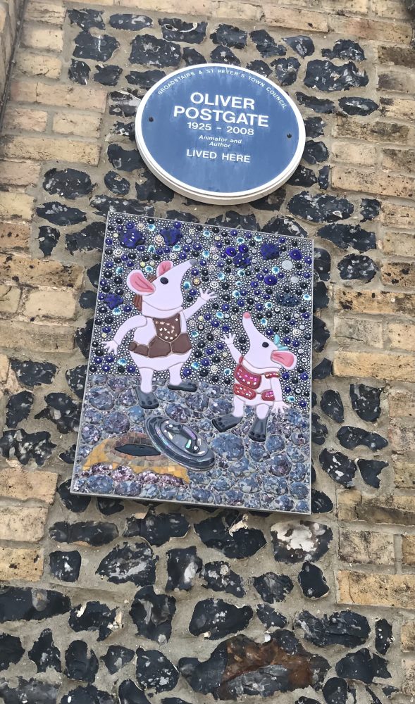 Blue plaque reads Oliver Postgate 1925 to 2008 animator and author lived here. 

Underneath plaque mosaic of two clangers puppets.