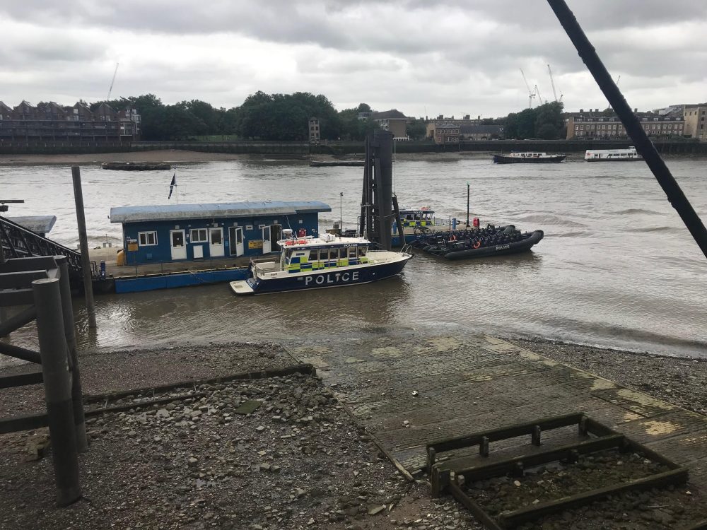 Police boat and speedboats around a thames pontoon dock. Sky grey and weather cloudy