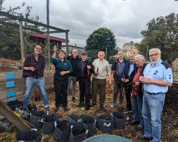 Group poses with gardening equipment and hop plants