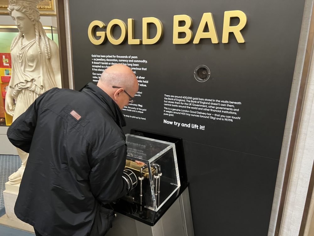 Wide shot photo of a Geezer holding a gold bar.